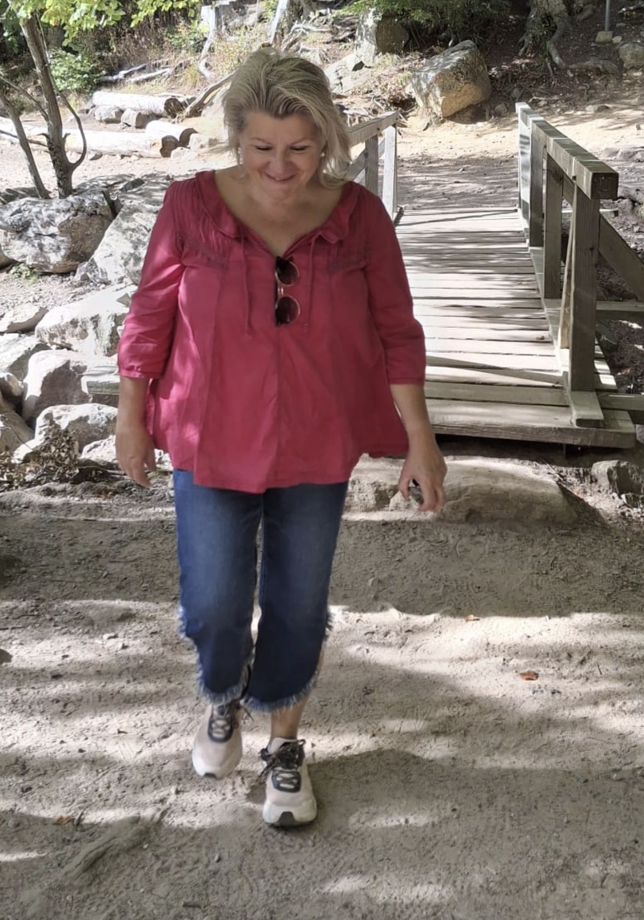 Franziska Hofstetter geht lächelnd über einen sonnigen Weg mit einer Holzbrücke im Hintergrund